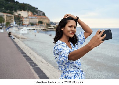 Beautiful smiling young woman takes selfie with a smartphone at the Promenade des Anglais in Nice, France - Powered by Shutterstock