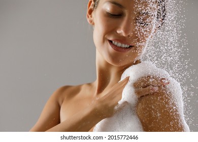 Beautiful smiling young woman taking a shower. Water drops and bath foam on her shoulder