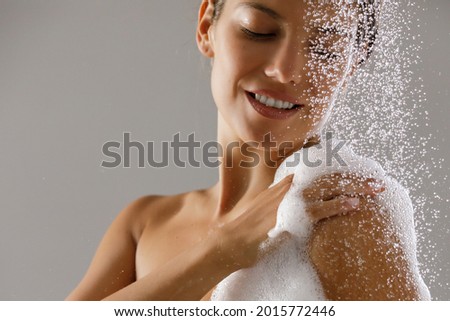 Beautiful smiling young woman taking a shower. Water drops and bath foam on her shoulder
