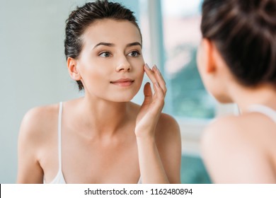 Beautiful Smiling Young Woman Touching Face And Looking At Mirror In Bathroom 