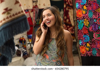 Beautiful Smiling Young Woman Using Her Celphone, Andean Traditional Clothing Textile Yarn And Woven By Hand In Wool, Colorful Fabrics Background