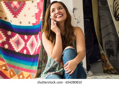 Beautiful Smiling Young Woman Using Her Celphone, Andean Traditional Clothing Textile Yarn And Woven By Hand In Wool, Colorful Fabrics Background