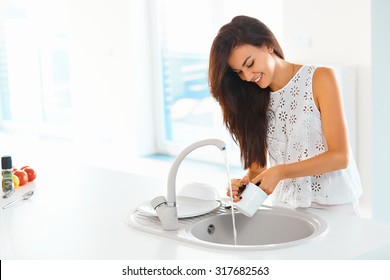 Beautiful smiling young woman washing a cup in white kitchen. 