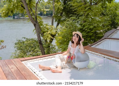 Beautiful smiling young woman wearing hat playing with pet on mesh seat near the nature lake view. relaxing time on summer holiday vacation. Leisure, travel, tourism with cute small prairie dog.