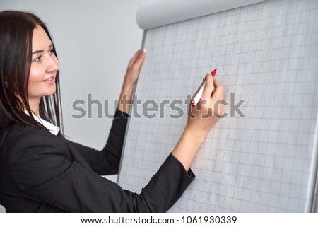 Beautiful smiling young woman writing on a blank flipchart in office as she does a presentation or promotion