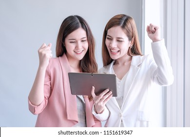 Beautiful smilling happily asian businesswomen in suit jacket using ipad in modern office. Joyful,relaxing Asian working girls. Technology,business concept. Cheerful asian women.
