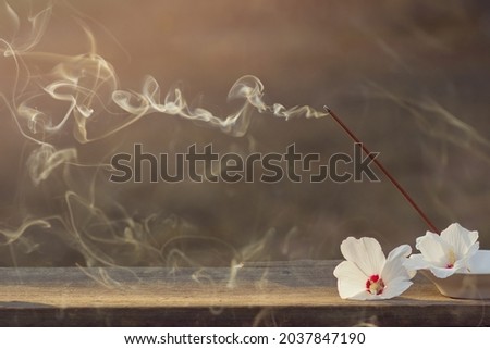 Beautiful smoke from incense sticks and burning incense with white flowers in a bowl on a wooden table outdoors. Background for design. Spiritual practices, meditation. Copyspace