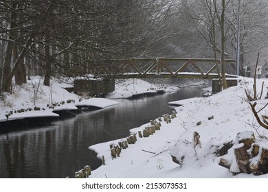 A Beautiful Snowy View Of A Wooden Bridge Above The River With Ice On The Sides And Snow Along The Edge