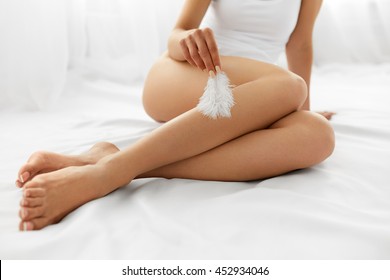Beautiful Soft Skin. Closeup Of Long Woman Legs With Perfect Hairless Smooth And Silky Skin, Woman's Hand Touhing Her Sexy Slender Leg With White Feather. Hair Removal, Beauty Body Care Concepts