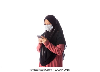 Beautiful southeast asian muslim female in hijab wearing face mask using a smartphone to communicate and reading news isolated over white background.