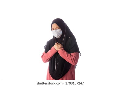 Beautiful southeast asian muslim female in hijab wearing face mask holding her hands near the chest with worry, sad and hurt facial expression isolated over white background.