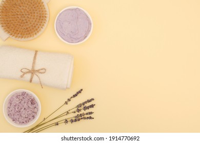 Beautiful Spa Composition With A Brush For Dry Anti-cellulite Body Massage, Sea Lavender Bath Salt, Natural Sea Salt Scrub, White Towel, Lavender Sprigs On A Yellow Background With Copy Space. The