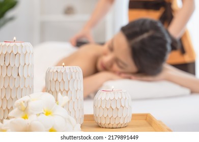 Beautiful spa composition with candles and frangipani flower. Blurred figures of woman enjoying hot stone massage and masseur in background.