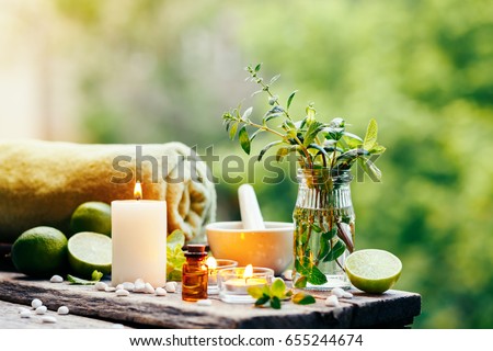 Beautiful spa composition with essential oil, fresh peppermint and burning candles on wooden table outdoors. Selective focus.