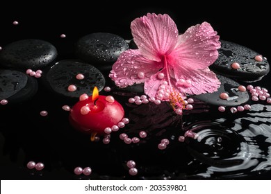 Beautiful spa setting of delicate pink hibiscus, zen stones with drops, candle and pearl beads on ripple water,  closeup