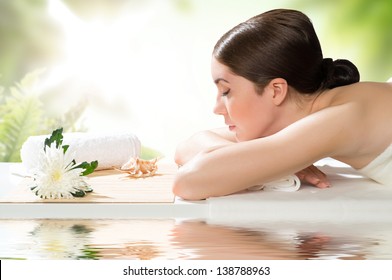 Beautiful Spa Woman Lying On The Couch, In Front Of Her Flower And Rolled Towel