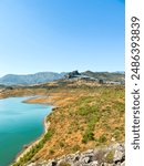 A beautiful Spanish Pueblo Blanco atop a hillside overlooking a lake in Southern Andalusia. blue sky and dry hillsides of cork and olive trees.