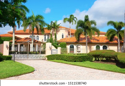 Beautiful Spanish style luxury mansion residential home with a privacy gate and palm trees on a blue sky sunny morning.