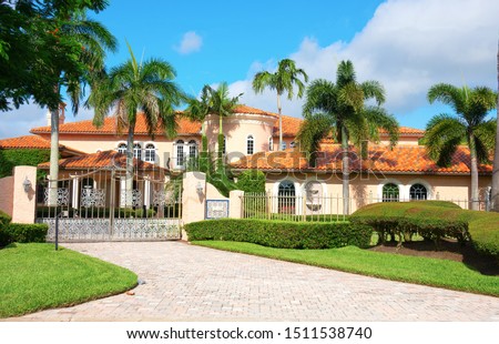Beautiful Spanish style luxury mansion residential home with a privacy gate and palm trees on a blue sky sunny morning.