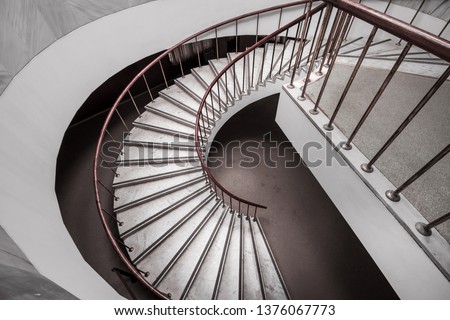 Beautiful spiral white marble staircase with dark red wooden balustrade. Spiral stairway case. Common stone office curved steps. Side view from above.Curved stairs lead down.