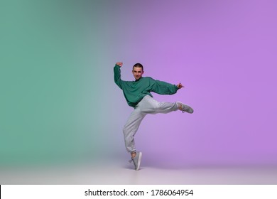 Beautiful sportive boy dancing hip-hop in stylish clothes on colorful gradient background at dance hall in neon light. Youth culture, movement, style and fashion, action. Fashionable bright portrait.