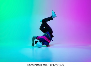 Beautiful sportive boy dancing hip-hop in stylish clothes on colorful gradient background at dance hall in neon. Youth culture, movement, style and fashion, action. Fashionable bright portrait.