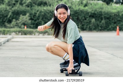 Beautiful sportive hipster happy Asian woman wearing casual shirt and shorts with headphone to listen music while playing skateboard as hobby in free time day on holiday, smiling at outdoor park - Powered by Shutterstock