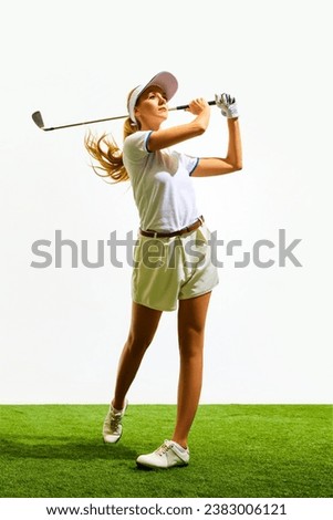 Beautiful, sportive, young blonde girl in white shorts and t-shirt playing golf on grass, teeing off isolated over white background. Concept of sport, hobby, beauty and fashion, relaxation, game