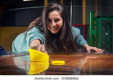 Beautiful sports girl plays air hockey in the entertainment center. Children's park. Family holiday. Mixed media