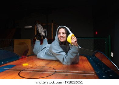 Beautiful sports girl plays air hockey in the entertainment center. Children's park. Family holiday. Mixed media