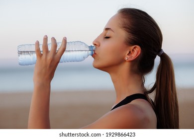 beautiful sports girl in a top and sneakers on a morning run drinks water from a bottle