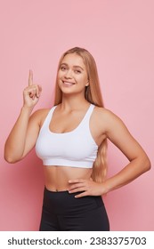 Beautiful sportsgirl with long blondehair posing in pink studio pointing finger up, Beauty and Health concept, copy space