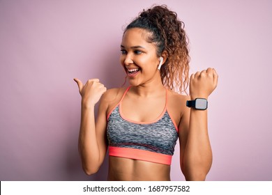 Beautiful sportswoman with curly hair doing sport wearing sportswear using smartwatch pointing and showing with thumb up to the side with happy face smiling
