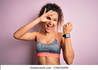 Beautiful sportswoman with curly hair doing sport wearing sportswear using smartwatch with happy face smiling doing ok sign with hand on eye looking through fingers - Shutterstock ID 1768196909