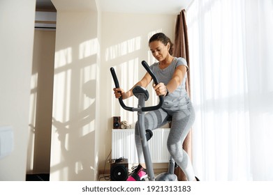 Beautiful sportswoman cycling a bike at home. Cardio training, exercising legs, Cardio workout at home - Shutterstock ID 1921313183