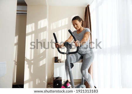 Beautiful sportswoman cycling a bike at home. Cardio training, exercising legs, Cardio workout at home