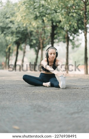 A beautiful sportswoman in sportswear is stretching her body with a smile on her face, while doing flexibility exercises to warm up before a running workout in Autumn city park background