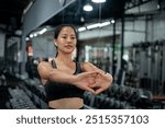 A beautiful, sporty Asian woman in athletic wear is stretching her arms, warming up before her workout in the gym. workout, exercise, training, healthy lifestyle