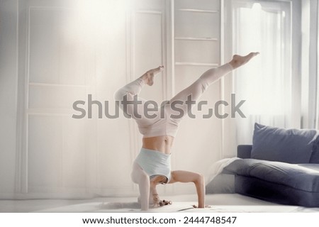 Beautiful sporty fit woman practicing yoga handstand asana, Light-filled room, sporty woman excels in her stretching routine.