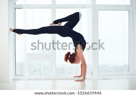 Beautiful sporty fit yogi redhead woman practices yoga handstand asana Bhuja Vrischikasana - Scorpion pose at the yoga studio.
