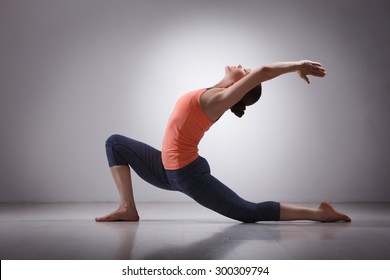 Beautiful sporty fit yogini woman practices yoga asana  Anjaneyasana - low crescent lunge pose in surya namaskar in studio