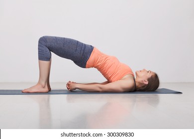 Beautiful sporty fit yogini woman practices yoga asana setu bandhasana - bridge pose variation in studio
