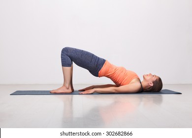 Beautiful sporty fit yogini woman practices yoga asana setu bandhasana - bridge pose beginner variation in studio