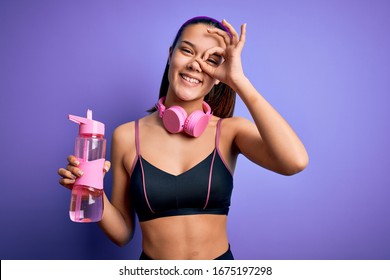 Beautiful Sporty Girl Doing Sport Using Headphones Drinking Bottle Of Water To Refreshment With Happy Face Smiling Doing Ok Sign With Hand On Eye Looking Through Fingers