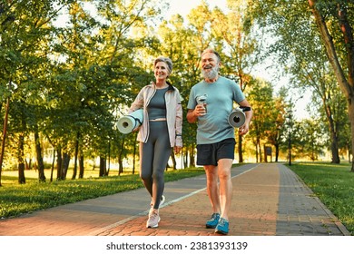 Beautiful sporty healthy active cheerful smiling middle-aged couple going to workout outdoors in park holding mats for yoga, pilates, gym. Sports healthy lifestyle. Friends on a morning walk. - Powered by Shutterstock