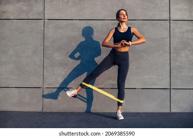 Beautiful sporty woman doing exercises with resistance band, fitness woman doing leg exercises with yellow fitness rubber band on gray background - Powered by Shutterstock