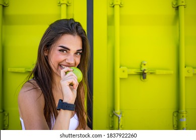 Beautiful sporty woman eating apple while resting from exercise. Healthy snack for fitness girl. Woman sitting and eating apple after workout. Young woman after sport workout eating apple
