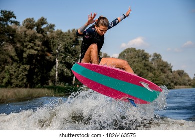 beautiful sporty woman in swimsuit and vest skillfully jumping over splashing river wave on bright surf style wakeboard.