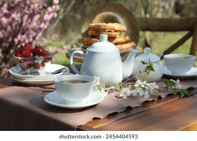 Beautiful spring flowers, freshly baked waffles and ripe strawberries on table served for tea drinking in garden - Powered by Shutterstock