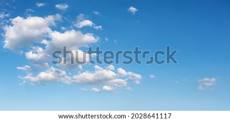 Beautiful spring sky with few white fluffy clouds on a sunny day. Clear bright blue summer sky for weather forecast, vacations and travel season ideas. Sky only panoramic image. Wide azure skyscape. 